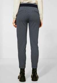 Marinblå byxor med diamantmönster, som har en elastisk midja och en smal passform, i kombination med svarta kraftiga kängor.