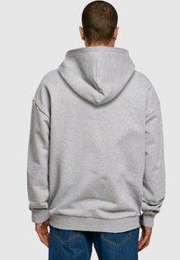 Grå hettegenser med oversized passform og ribbede mansjetter. Myk tekstur og synlig detalj med enkelt bakseam. Brukt med blå jeans.