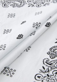 White fabric featuring black paisley and geometric patterns, with a smooth texture and folded in a way that showcases the designs.