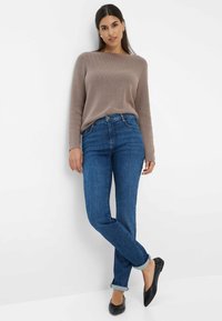 Maglione beige a maglia con texture a costine, jeans blu a vita alta e ballerine nere. Il maglione ha un collo a barca e maniche lunghe.