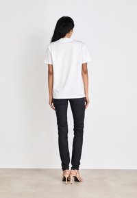 Vit kortärmad t-shirt, lös passform, mjukt bommaterial. Kombinerad med mörka skinny jeans och beige högklackade sandaler. Enkelt mönster.