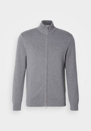 Pull zip gris avec un col montant, des poignets et un ourlet côtelés. Présente un petit logo sur la poitrine. Fabriqué à partir d'un tissu doux et texturé.