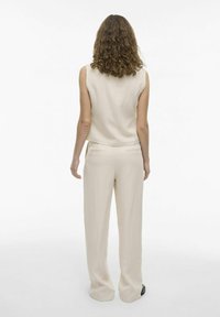 Beige mouwloos topje, gecombineerd met bijpassende wijde broek, beide gemaakt van lichtgewicht stof. De achterkant toont een gladde textuur en maatwerk snits.
