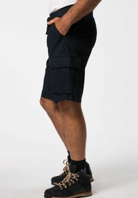 Pantalones cortos de carga azul marino con bolsillos laterales, un ajuste relajado y una tela texturizada, combinados con botas negras con cordones y detalles en dorado.