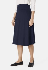 Gonna al ginocchio blu navy in morbido tessuto elasticizzato con una vita liscia, caratterizzata da una silhouette svasata e una texture sottile. Si indossano delle scarpe basse nere.
