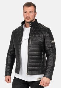 Zwarte leren jack met hexagonaal gestikte patroon, ritssluiting aan de voorkant en zakken, hoge kraag en logo accent op de mouw.