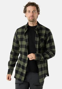 Zwart en groen geruite flanellen overhemd, met een knoopsluiting en lange mouwen, voorzien van een borstzak en textuurstof. Zwarte T-shirt eronder.