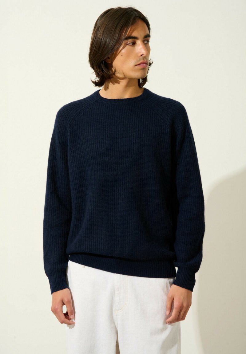 Marineblauer Rippstrickpullover mit Rundhalsausschnitt und langen Ärmeln. Verfügt über eine lockere Passform und einen strukturierten Stoff. Kombiniert mit hellen Hosen.