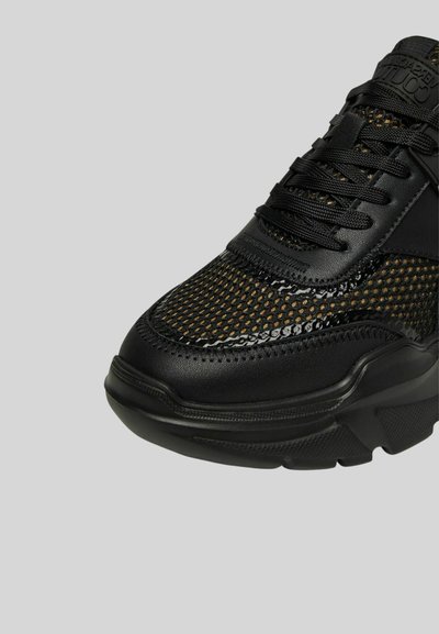 Scarpa sportiva nera con tomaia in rete e dettagli lucidi, linguetta imbottita e suola in gomma spessa. Dettagli testurizzati su tutta la superficie.