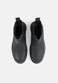 Botas de cuero negras hasta el tobillo con paneles elásticos laterales, punta redonda y detalles texturizados en la parte superior. Suela plana con costuras sutiles.