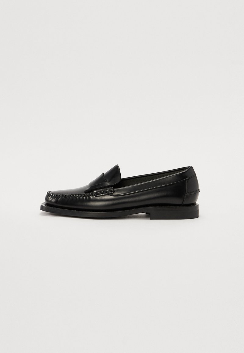 Mocassins en cuir noir avec une finition lisse, présentant un design cousu, un petit talon et un bout arrondi, mettant en valeur une silhouette classique.