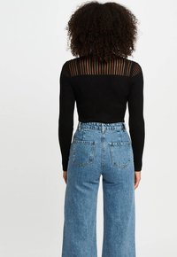 Maglietta nera a maniche lunghe a coste con schiena strizzata trasparente, abbinata a jeans a vita alta blu chiaro a gamba larga con due tasche posteriori.