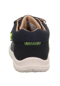 Marineblaue Sneaker mit einem strukturierten Obermaterial, kontrastierenden gelb-grünen Akzenten, gepolstertem Kragen und weißer Gummisohle mit Griff.