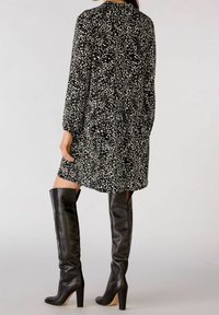 Czarna sukienka w leopardzie z kremowymi akcentami, z długimi rękawami, w połączeniu z czarnymi skórzanymi botkami na wysokim obcasie do kolan. Teksturowany materiał, luźny krój.