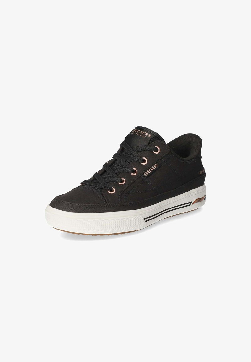 Baskets basses Skechers noires avec semelle blanche, lacets noirs et œillets ainsi que détails de marque en or rose.