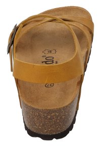 Sandalias cruzadas en piel de color mostaza con una plantilla de corcho y una suela de goma negra texturizada. Incluyen un detalle de hebilla metálica.
