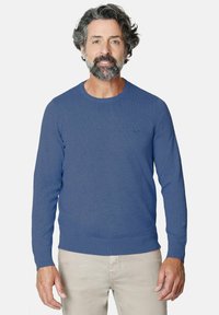Suéter azul de cuello redondo hecho de un suave tejido de punto. Presenta puños y dobladillo de canalé, con un sutil detalle de logo en el pecho.