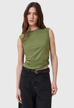 Top verde senza maniche con colletto rotondo; tessuto morbido e liscio; design aderente. Indossato con pantaloni neri a vita alta e una cintura nera con accessori dorati.