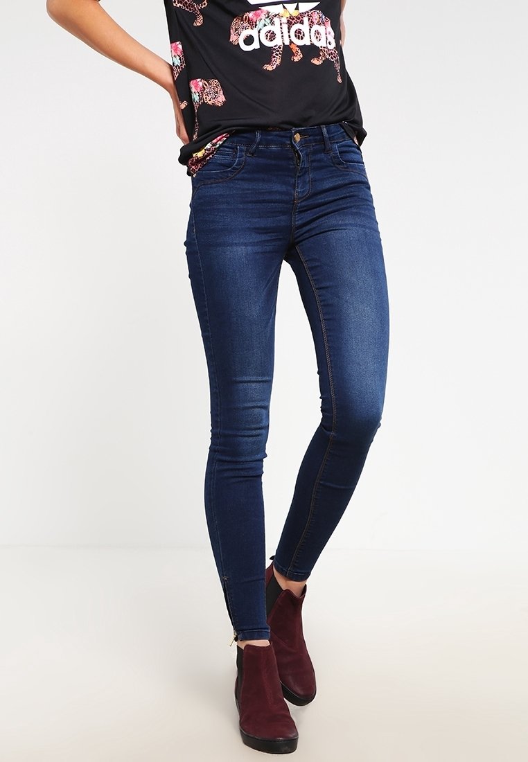 Jeans ajustados de mezclilla azul oscuro, con una textura suave, cintura alta y sutiles detalles de costura. Combinados con botas de tobillo burdeos.