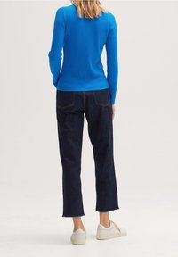 Geribbelde lange mouw top in felblauw, gecombineerd met donkere denim, cropped rechte jeans en witte sneakers met minimale details.