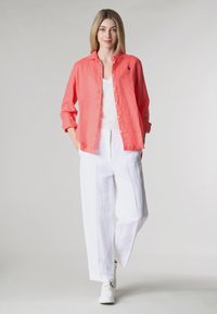 Una camicia button-up in lino corallo sopra un top bianco, abbinata a pantaloni larghi in lino bianchi e sneakers bianche; design semplice e vestibilità rilassata.
