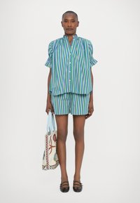 Camisa de botones a rayas y pantalones cortos en tonos azules, verdes y morados. Incluye mangas con volantes y una bolsa tote única bordada.