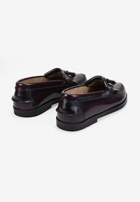 Zapatos de cuero burdeos oscuros con diseño de mocasín, que cuentan con borlas decorativas, detalles de costura y suela de goma negra.