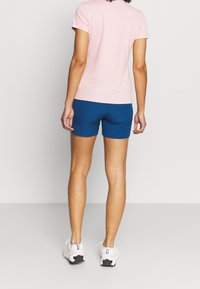 Camisa de manga corta rosa y pantalones cortos azules, con una textura suave. Zapatillas deportivas blancas con acentos negros. Diseño simple y funcional.