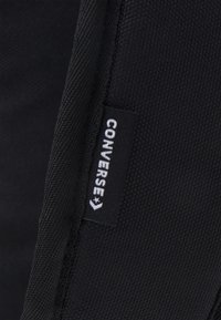 Botte noire en toile avec une texture. Présente une étiquette blanche "CONVERSE" cousue sur le côté, soulignant l'identité de la marque.