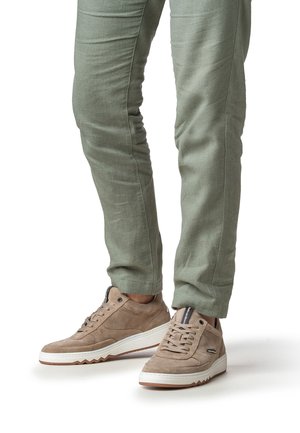 Beige suède sneakers met witte rubberen zool en textuurdetail; gedragen met lichtgroene slim-fit broek.