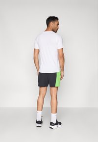 Αθλητική εμφάνιση ανδρών: λευκό κοντομάνικο μπλουζάκι με στρογγυλή λαιμόκοψη, συνδυασμένο με σκούρα σορτς που διαθέτουν φωτεινή πράσινη λεπτομέρεια.