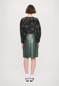 Černá halenka s květinovým vzorem a dlouhými rukávy, doplněná zelenou koženou pouzdrovou sukní. Má hladkou texturu a přiléhavý střih.