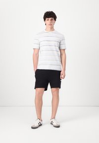 Lys gråstripet T-skjorte med rund hals, svarte shorts med sidelommer, og hvite sneakers med grå detaljer. Uformell atletisk bekledning.