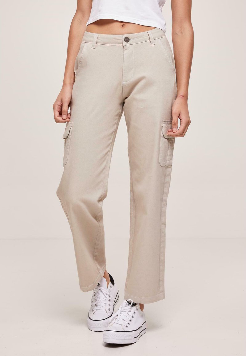 Beige cargo bukser med lige ben, med sidelommer, knaplukning og bæltestropper, parret med hvide sneakers.