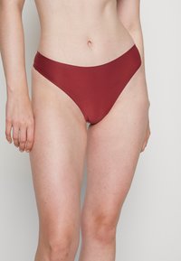 Parte de baixo de bikini em um vermelho profundo, feita de um tecido suave, apresentando um design de corte alto e cobertura mínima nas laterais.