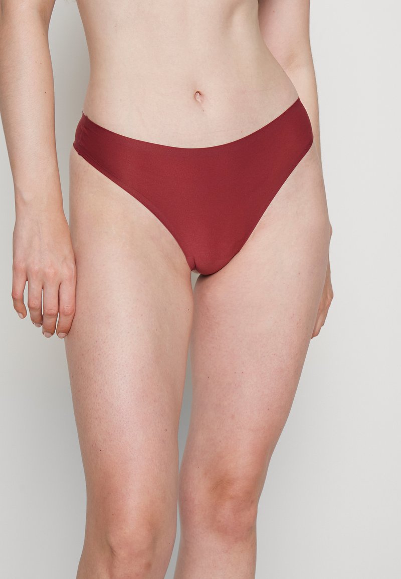 Parte de baixo de bikini em um vermelho profundo, feita de um tecido suave, apresentando um design de corte alto e cobertura mínima nas laterais.