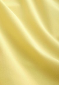 Tissu jaune lisse avec des plis doux et un léger éclat, mettant en valeur sa texture soyeuse et ses douces réflexions de lumière.
