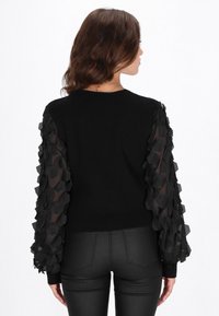 Maglione nero con maniche in tessuto trasparente nero arricciato e testurizzato. Design aderente, materiale a coste, scollo rotondo e retro liscio.