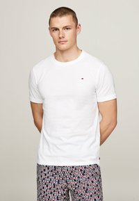 Hvid bomulds T-shirt med korte ærmer, rund hals og et lille broderet logo. Kombineret med mønstrede shorts med gentaget tekstdesign.