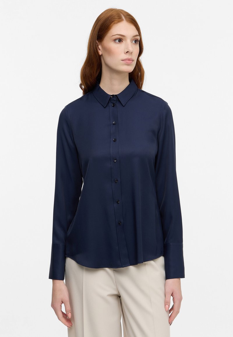 Navyblauwe zijden blouse met lange mouwen, een puntige kraag, knopen aan de voorkant en een ontspannen pasvorm. Gladde textuur met een glanzende afwerking.