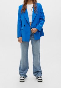 Blå överdimensionerad blazer med svarta knappar, ihop med ljusblå vida jeans och svart-vita sneakers. En kortärmad vit topp under.