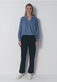 Blusa blu a maniche lunghe con scollo a V, abbinata a pantaloni neri a gamba larga. L'outfit è completato da sneakers bianche.