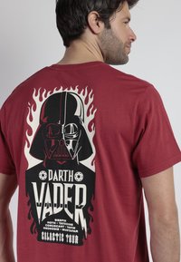 Camiseta roja de algodón con un gran gráfico en blanco y negro de Darth Vader, con acentos de llamas y el texto "Darth Vader Galactic Tour" debajo.