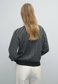 Black and gray striped sweater with a ribbed hem, long sleeves, and a relaxed fit, paired with white pants. Textured knit fabric.