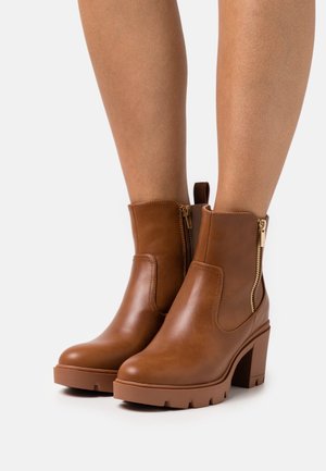 Hnědé kožené kotníkové boty s robustním podpatkem, vybavené postranními zipy a texturovanou podrážkou. Hladký povrch s minimálními švy.