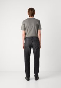 Camiseta de algodón gris con mangas cortas, combinada con jeans de mezclilla negros de corte recto y un sutil desvanecimiento. Unos zapatillas negras completan el look.