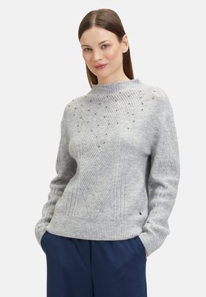 Pull en tricot gris avec un col montant, présentant un motif en chevrons texturé et de petits embellissements. Poignets et ourlet côtelés.