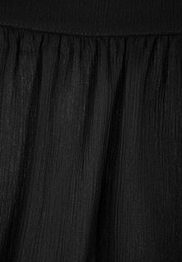 Tissu plissé noir avec une finition légère et texturée. La surface présente de fines lignes verticales et une ceinture lisse.