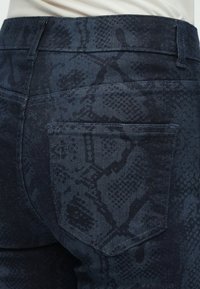 Donkere denimjeans met een slangenprinttextuur. De stof heeft een gladde afwerking met subtiele stiksel details en een achterzak.