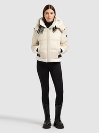 Pikowana beżowa kurtka z kapturem wykończonym futerkiem, kontrastowymi czarnymi paskami i przednimi kieszeniami. Modelka ma na sobie czarne legginsy i wojskowe buty.